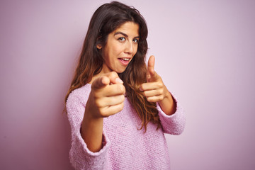 Young beautiful woman wearing sweater standing over pink isolated background pointing fingers to camera with happy and funny face. Good energy and vibes.