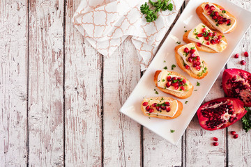 Holiday crostini appetizers with brie cheese, pomegranates and parsley. Above view table scene...