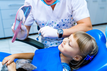 male dentist holding mirror in front of little girl patient. Lovely little kid looking in the...