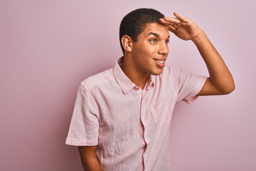 Young handsome arab man wearing casual shirt standing over isolated pink background very happy and smiling looking far away with hand over head. Searching concept.