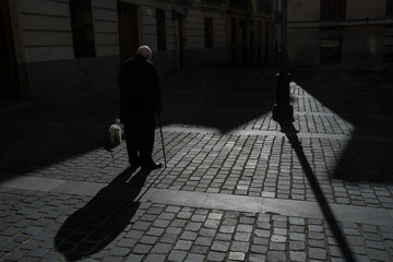  silhouette of senior man with walking stick on his back over a shady area in Madrid, Spain