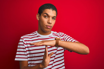 Young handsome arab man wearing striped t-shirt over isolated red background Doing time out gesture...