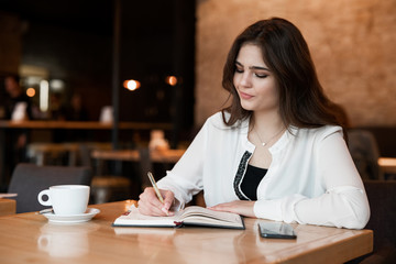 young beautiful woman working outside office taking notes in her planner while drinking hot coffee in the cafe multitasking modern businesswoman