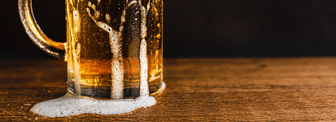 Cold beer with foam in a mug, on a wooden table and a dark background with blank space for a logo...