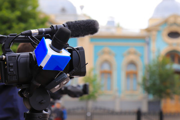 Television journalist with a microphone and a camera at a mass event, press conference. Blue microphone and equipment for television filming on a city street