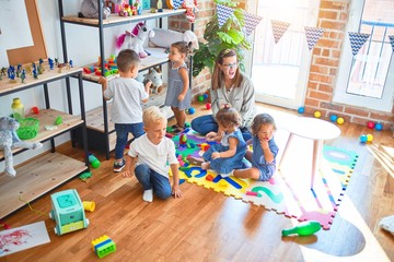 Beautiful teacher and group of toddlers playing around lots of toys at kindergarten