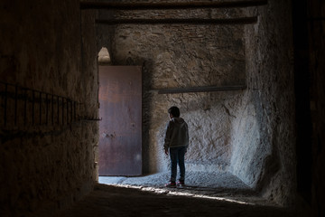 Obraz na płótnie Canvas boy with his back facing the light coming out a door in the castle of xativa