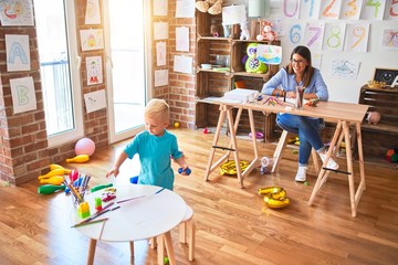 Young caucasian child playing at playschool with teacher. Young woman sitting on the desk of the classroom