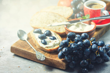 Whole grain bread toasts with ricotta cheese, black grapes on a wooden cutting board. Food concept. Selective focus.