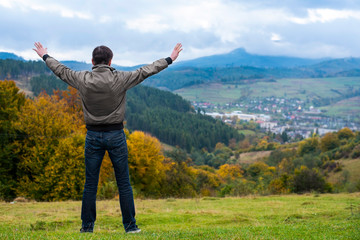 Man raising his hands stands near the forest on the outskirts of his city and is glad that he is finally coming home from work. The man prays and thanks God for his city