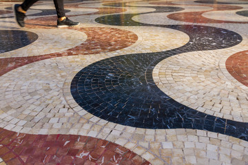 Detail of the Paseo de la Esplanada in Alicante with its characteristic mosaic of colored tiles and legs of young person passing 