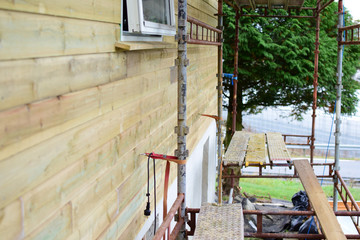 Fototapeta na wymiar Scaffolding is installed along the new wall of the wooden house. Concept: Overhaul and restoration of wooden houses.