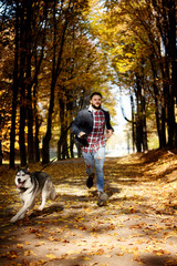 Naklejka na ściany i meble Hipster stylish guy with his husky dog in autumn forest.Run .Dynamic.Pedigree dog concept. Best friends. Unconditional love. Guy enjoy walk with husky dog. Siberian husky cool pet. Animal husbandry. 