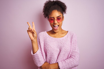 African american woman wearing winter sweater and sunglasses over isolated pink background smiling...