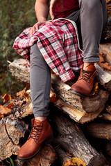 Man feet with brown leather boot, grey jeans, and red shirt in cage on the leg .Siting on pile of firewood
