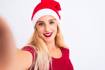 Woman wearing Christmas Santa hat make selfie by camera over isolated white background with a happy face standing and smiling with a confident smile showing teeth