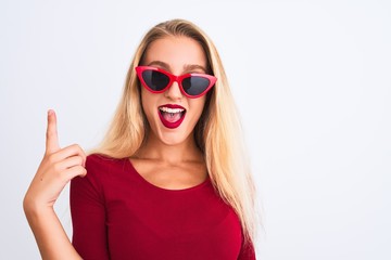 Young beautiful woman wearing red t-shirt and sunglasses over isolated white background pointing finger up with successful idea. Exited and happy. Number one.