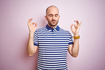 Fototapeta premium Young bald man with beard wearing casual striped blue t-shirt over pink isolated background relax and smiling with eyes closed doing meditation gesture with fingers. Yoga concept.
