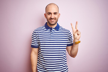 Fototapeta premium Young bald man with beard wearing casual striped blue t-shirt over pink isolated background showing and pointing up with fingers number two while smiling confident and happy.