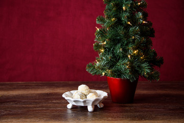 Christmas treat, white dish with Russian Tea Cake cookies on dark wood table with artificial Christmas tree with white lights, red background