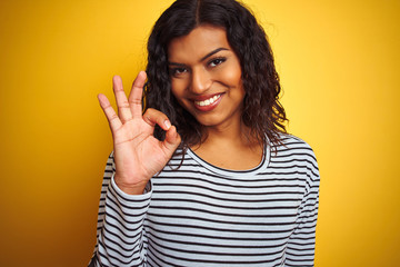 Transsexual transgender woman wearing striped t-shirt over isolated yellow background doing ok sign with fingers, excellent symbol