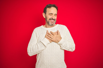 Handsome middle age senior man with grey hair over isolated red background smiling with hands on chest with closed eyes and grateful gesture on face. Health concept.