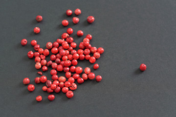 Whole pink red peppercorns on black gray paper, view from above