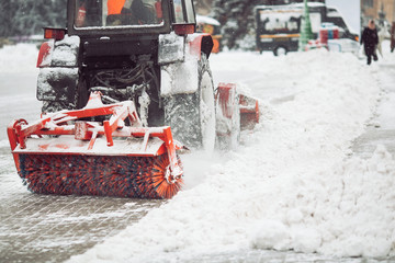 City service cleaning snow , a small tractor with a rotating brush clears a road in the city park from the fresh fallen snow on winter day, brush - close-up.