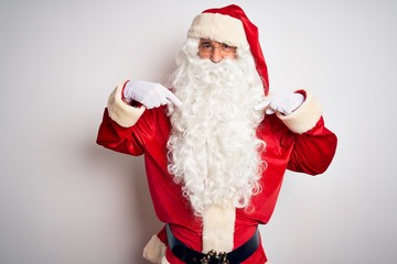 Middle age handsome man wearing Santa costume standing over isolated white background looking confident with smile on face, pointing oneself with fingers proud and happy.