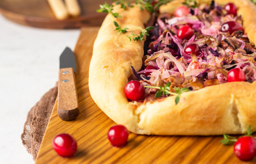 Homemade open pie with different types of cabbage, sauerkraut and cranberry on wooden cutting board. Selective focus. Vegetarian food.