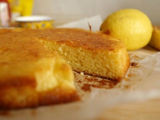 Closeup photo of a freshly baked lemon cake with one slice cut and taken away, with a bright yellow lemon in background. Homemade citrus cake.