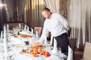 Waiter serving table in the restaurant preparing to receive guests.