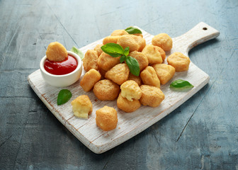 Fried mozzarella, cheddar cheese bites, balls with ketchup on white wooden board
