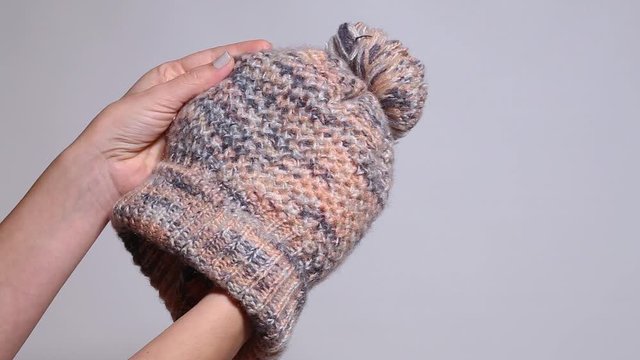 Closeup view of female hands holding warm pastel winter hat. Real time full hd video footage.