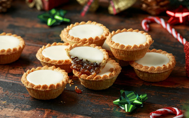 British Christmas iced mince pies with decoration, gifts, green tree branch on wooden rustic table
