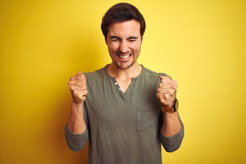 Fototapeta premium Young handsome man wearing casual t-shirt standing over isolated yellow background excited for success with arms raised and eyes closed celebrating victory smiling. Winner concept.