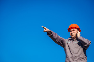Construction worker in a helmet against the blue sky talking on the phone. Contractor control...