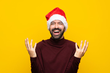 Man with christmas hat over isolated yellow background smiling a lot