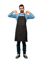Fototapeta premium Full-length shot of Man with apron showing thumb down over isolated white background