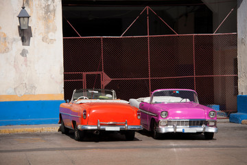 Dos coches clásicos americanos descapotables de los años 60 aparcados en la entrada de un garaje...