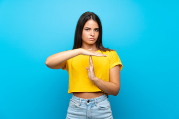 Young girl over isolated blue background making time out gesture