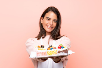 Young girl holding lots of different mini cakes over isolated background