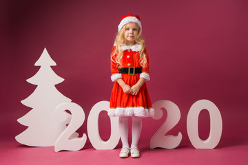 little girl in Santa costume stands with numbers 2020, space for text, new year 2020
