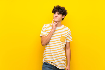 Young man over isolated yellow wall thinking an idea while looking up