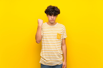 Young man over isolated yellow wall with angry gesture