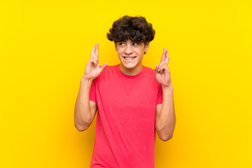 Young man over isolated yellow wall with fingers crossing