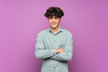 Young man over isolated purple wall keeping the arms crossed in frontal position