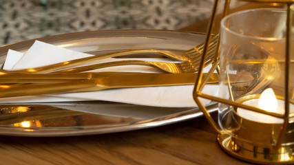 Gold cutlery on a silver tray ready for serving some food at breakfast, lunch or dinner next to a golden lamp