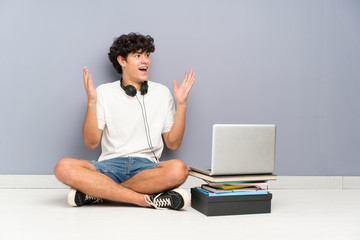Young man with his laptop sitting one the floor with surprise facial expression
