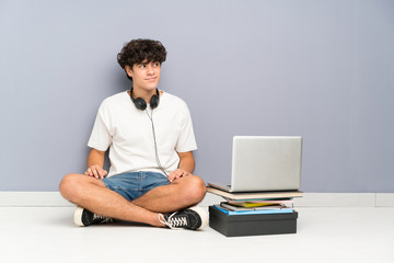 Young man with his laptop sitting one the floor standing and looking to the side